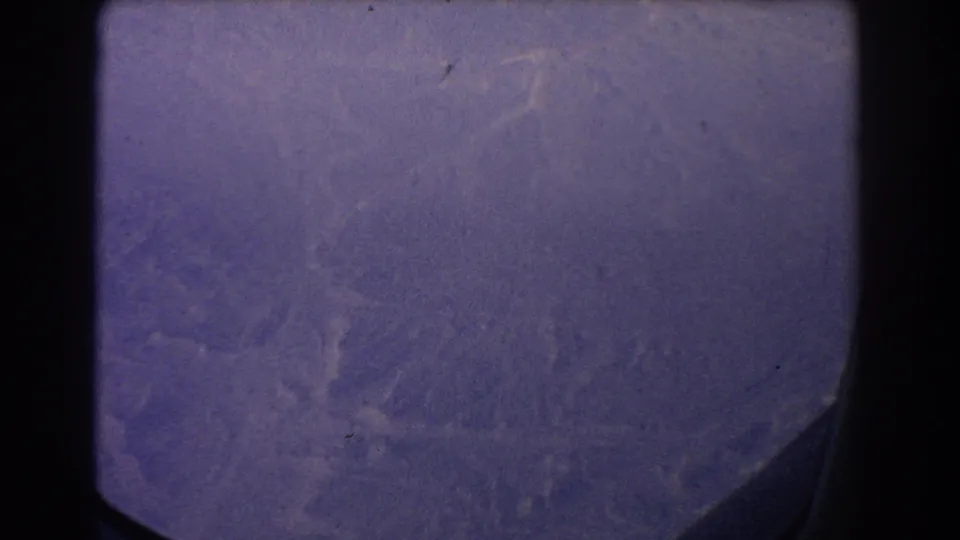 1967 Sydney-area 8mm frame showing an indistinct aerial landscape with mountain-like textures, film grain, scratches, and a dark corner edge.