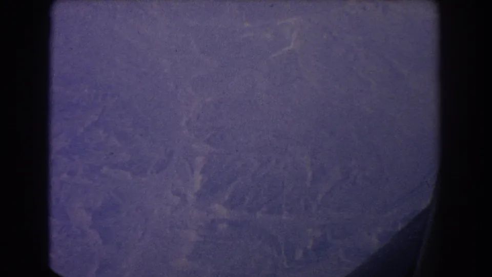 1967 8mm view near Sydney showing hazy trees and hills below an airplane window, with rounded frame edges and film wear.