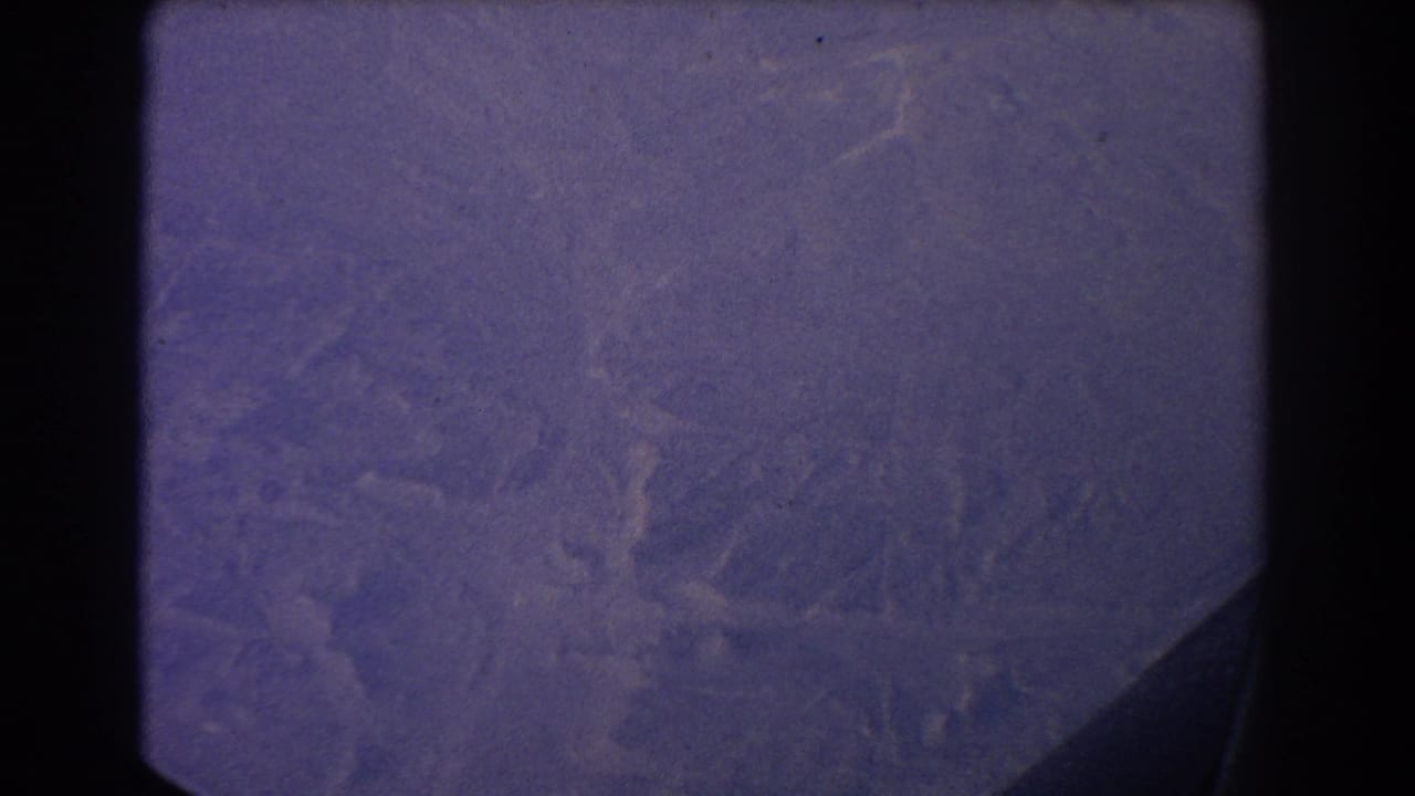 Hazy aerial view of wooded hills framed by a dark airplane window edge.