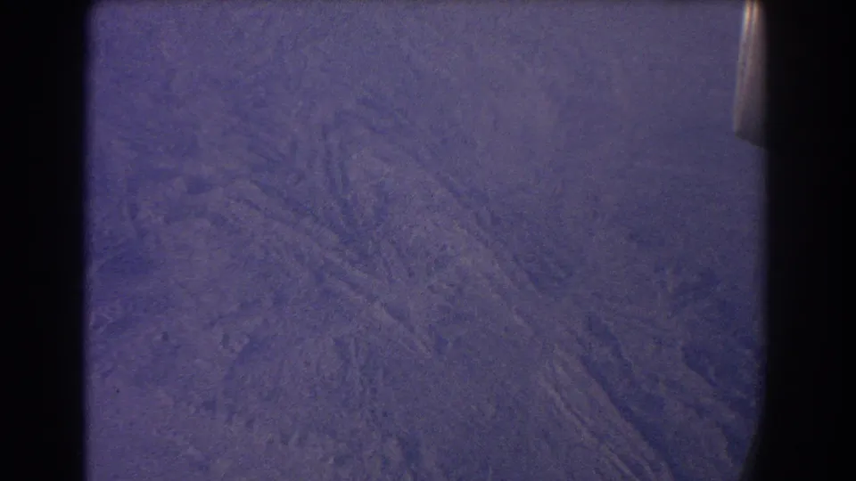 1967 8mm airplane-window view over arid Australian terrain with faint dry-channel textures and a purple color cast.