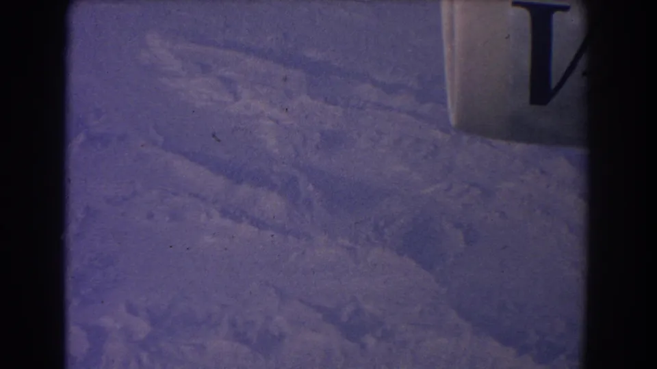 1967 8mm aerial view over arid Australian terrain, with faint surface patterns and a dark obstruction near the center.