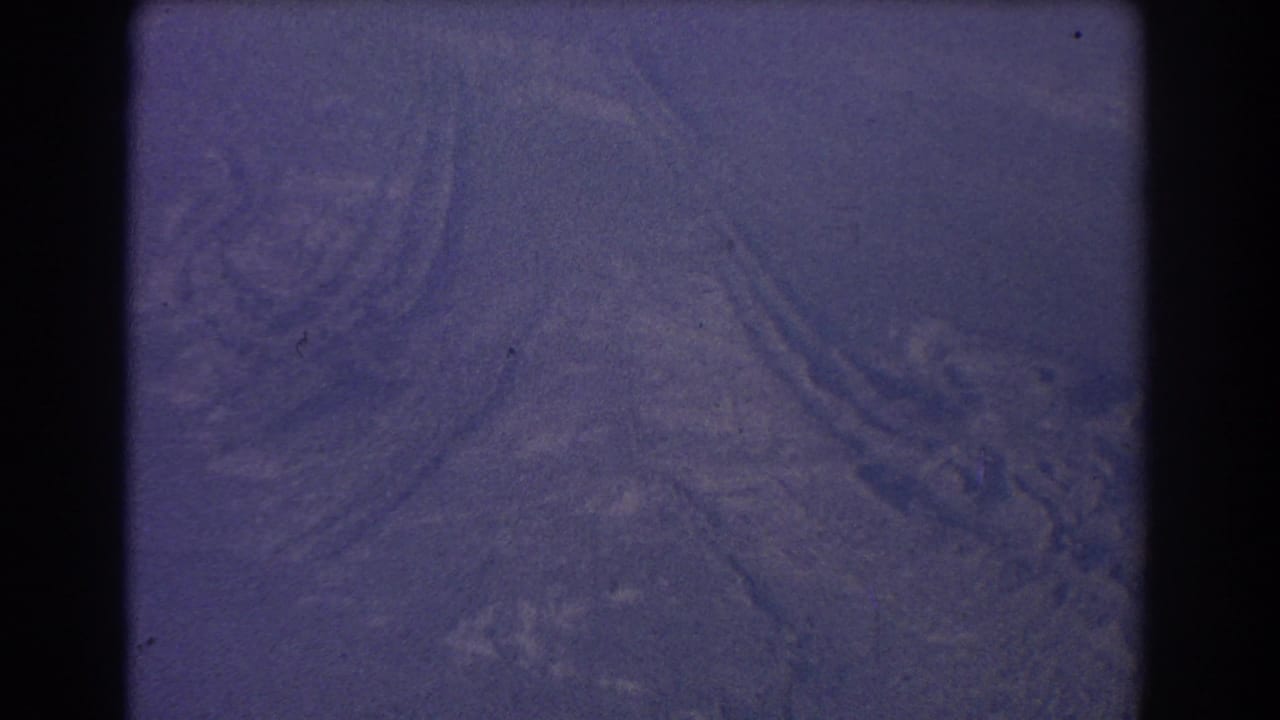 Soft aerial view of hazy terrain with winding pale lines and dark film borders.