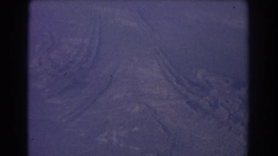 1967 8mm aerial frame showing dry landscape patterns below, softened by haze, grain, and purple-blue color shift.