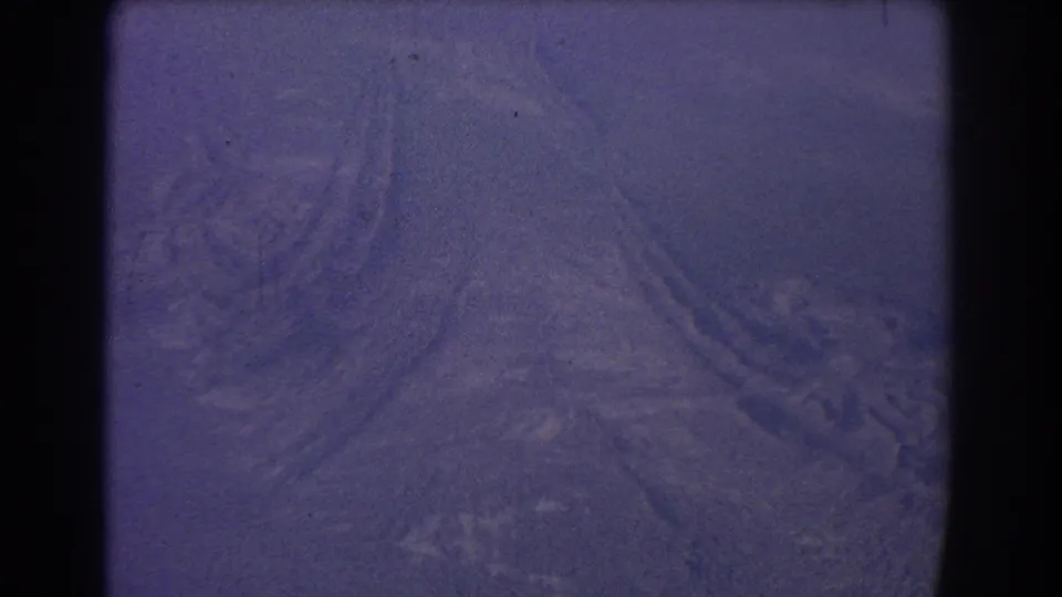 Vintage 8mm aerial view over arid terrain, with faint land forms visible beneath grain, dust, and a strong purple cast.