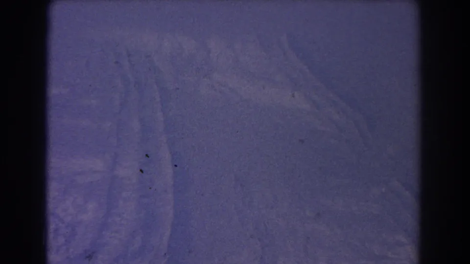 1967 8mm aerial frame over remote-looking terrain, with faint lines on the ground and visible dust specks in the scan.