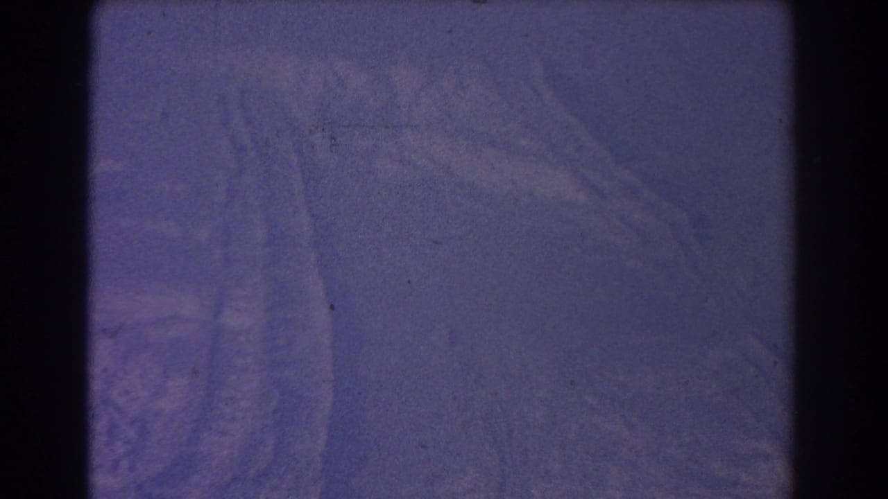 1967 8mm frame from Sydney metadata showing a purple-tinted snowy surface with faint track marks and visible film gate edges.