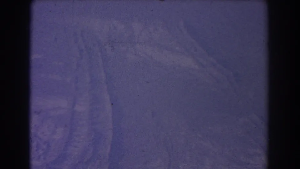1967 8mm frame from Sydney metadata showing a purple-tinted snowy surface with faint track marks and visible film gate edges.