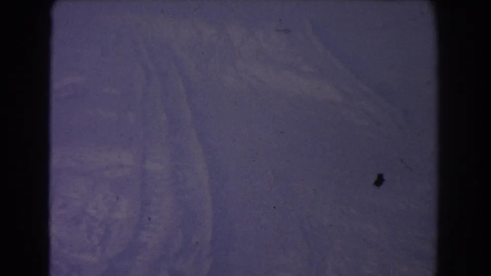 Final 8mm frame showing a softly exposed snowy surface with faint track marks, purple tint, grain, and visible film borders.
