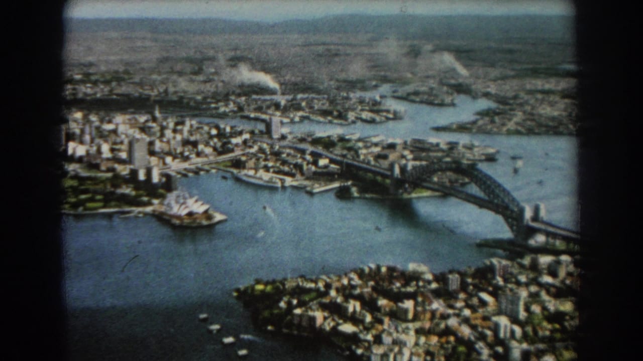 Aerial view of Sydney Harbour with Harbour Bridge, Opera House, city blocks, and water.