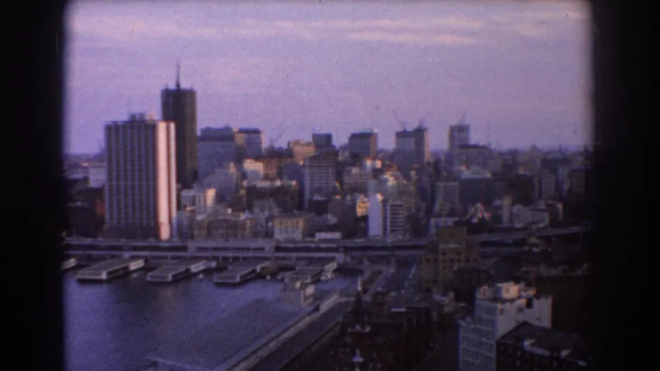 1967 Sydney skyline from above, with waterfront towers, wharves, cranes, and harbour water in the foreground.