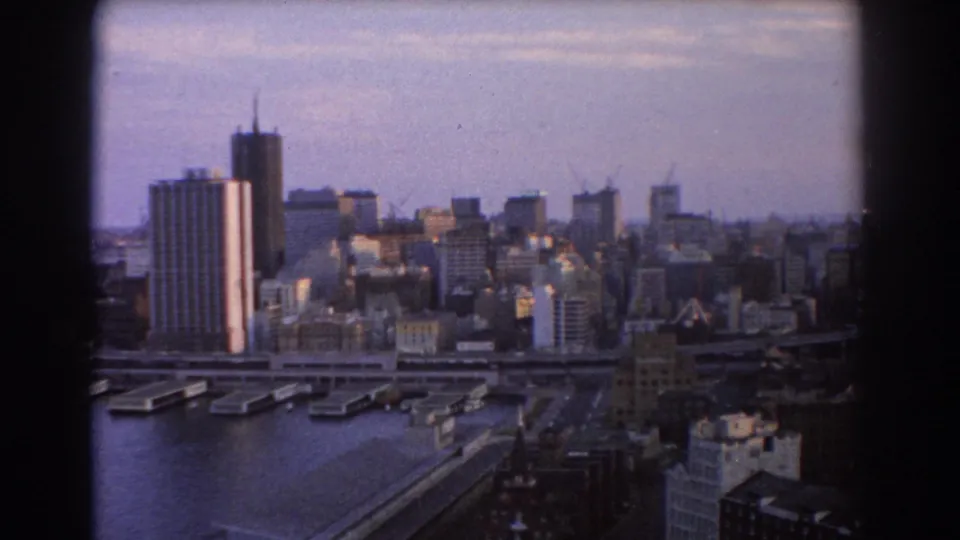1967 8mm view of Sydney's harbourfront cityscape, with towers, wharves, roadways, and distant construction cranes.