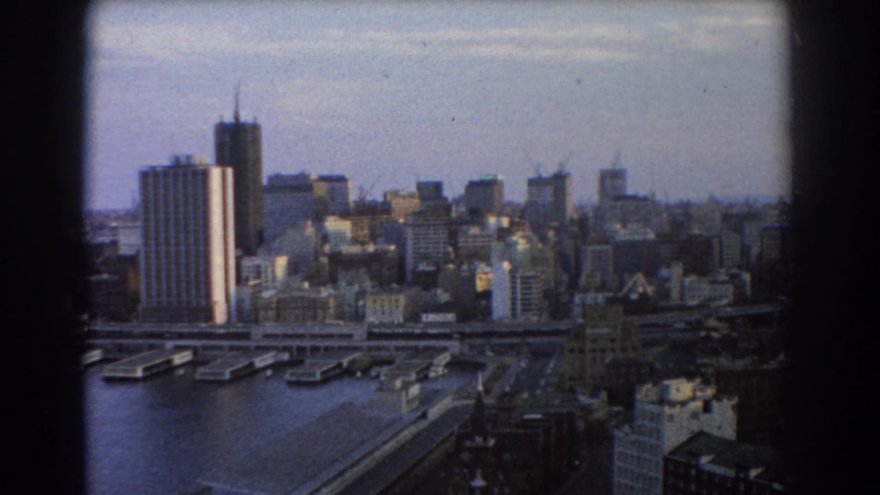 Elevated Sydney harbor cityscape with bridge, piers, and high-rise buildings.