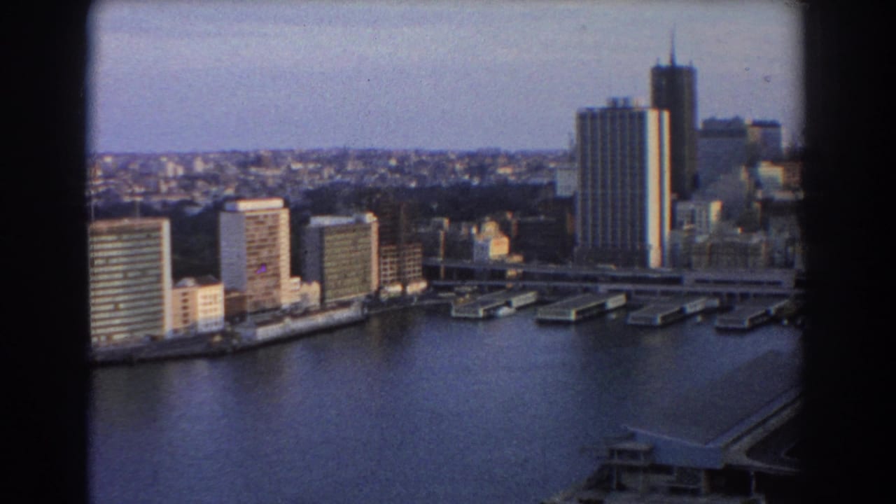 Elevated view over Sydney harbor water, waterfront buildings, piers, and a tall tower framed by dark film edges.