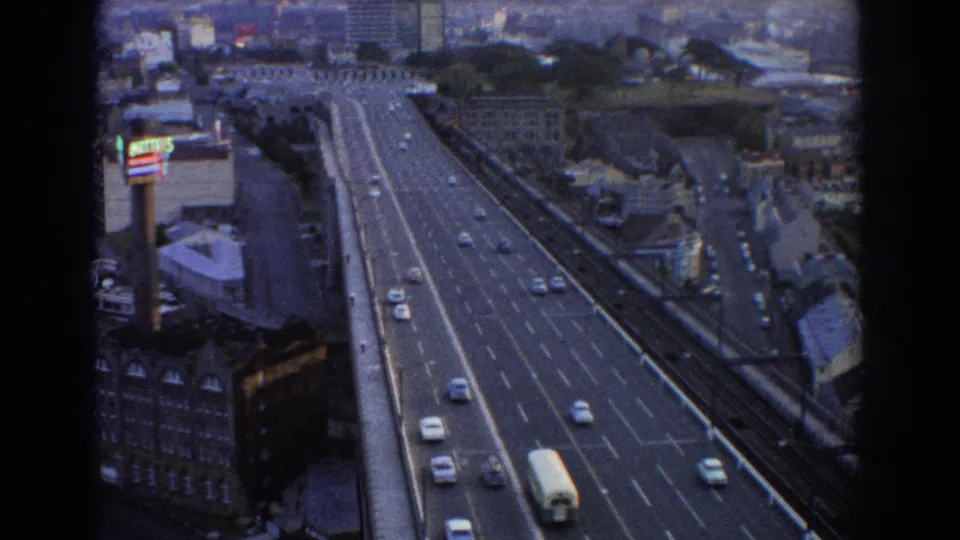 1967 Sydney 8mm frame showing cars and a white bus moving along an elevated multi-lane highway near city buildings.