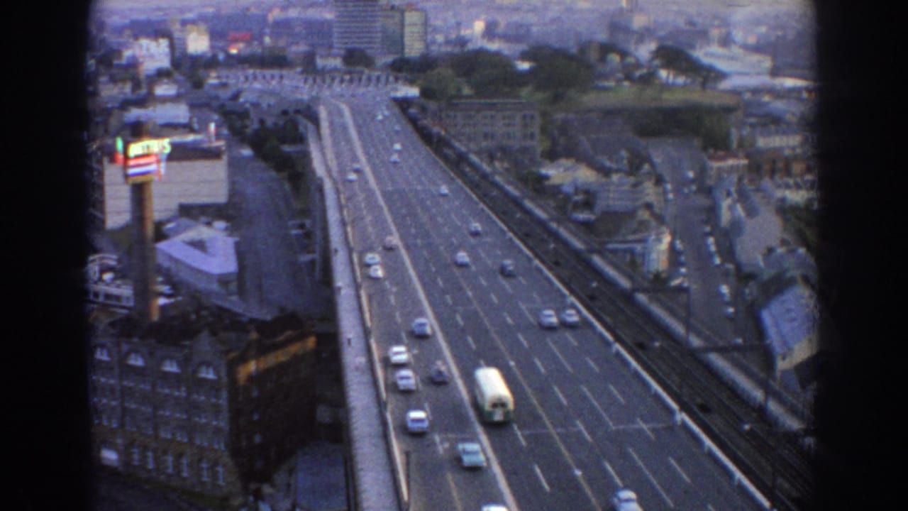 Traffic moves in both directions on a broad roadway beside urban buildings.