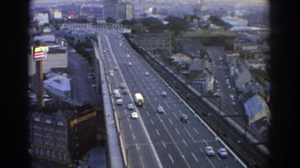 1967 Sydney 8mm still showing elevated roadway traffic, a white bus, multiple cars, city buildings, and dark film frame edges.