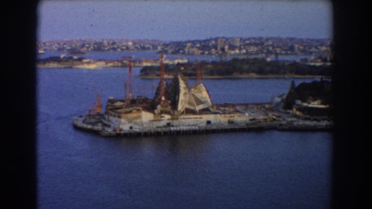 Sydney Opera House construction site across the harbour with cranes and skyline beyond.