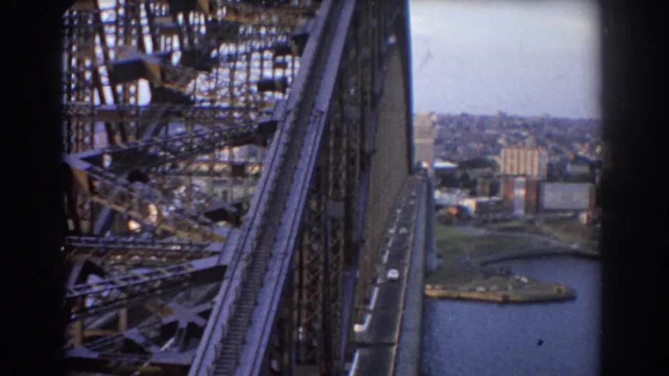 Sydney Harbour Bridge in 1967 seen from an elevated angle, with truss structure, traffic lanes, harbor, and city skyline.