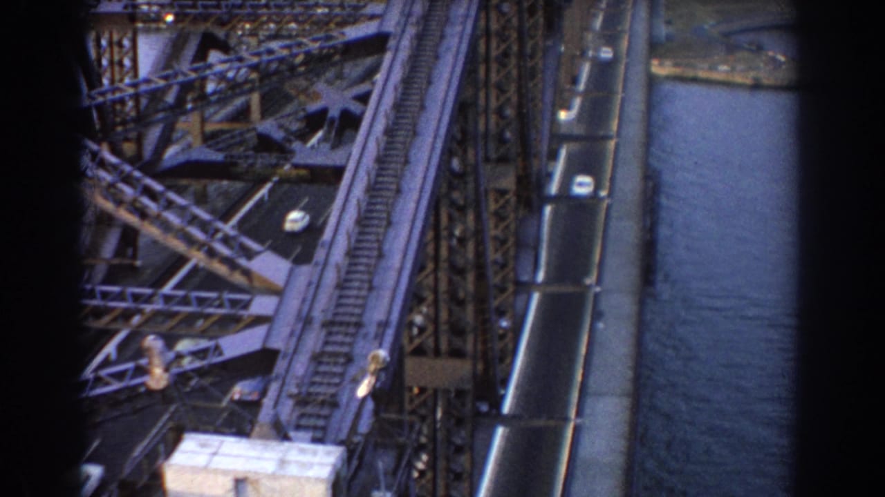 High-angle view of bridge traffic, steel trusswork, rail line, and water below.