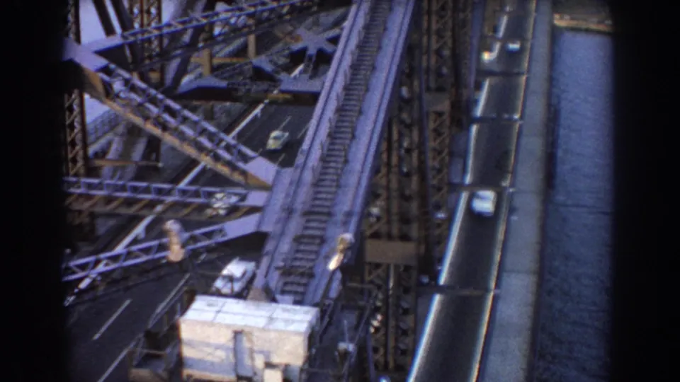Elevated 1967 Sydney bridge view with cars on the roadway and rail structure beside the harbor water.