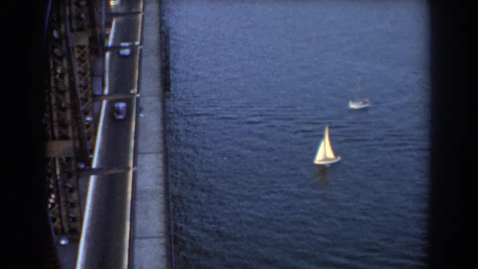 1967 Sydney 8mm frame showing sailboats on blue water below a steel truss bridge with cars moving along the edge.