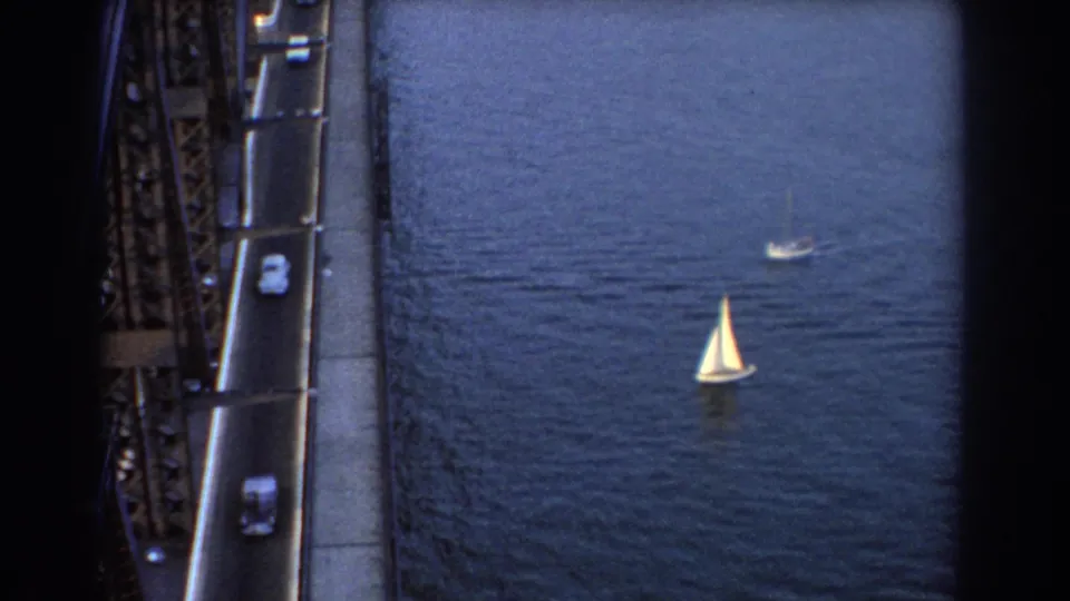 1967 Sydney 8mm frame with sailboats spread across the water and cars traveling along the steel bridge roadway.