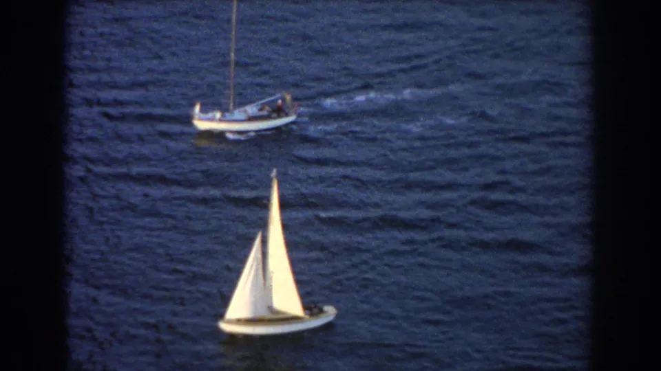 1967 Sydney 8mm frame with a foreground sailboat and another small boat moving across dark blue harbor water.