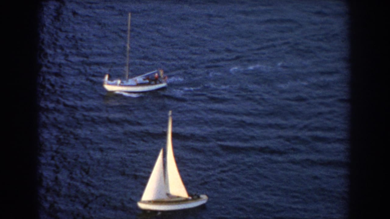 White-sailed boat below a larger craft on rippled water.