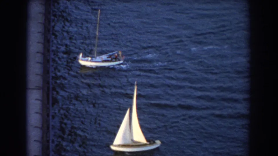 Elevated 8mm frame near Sydney showing a white-sailed boat, a larger craft, and a vertical dock or shoreline edge.