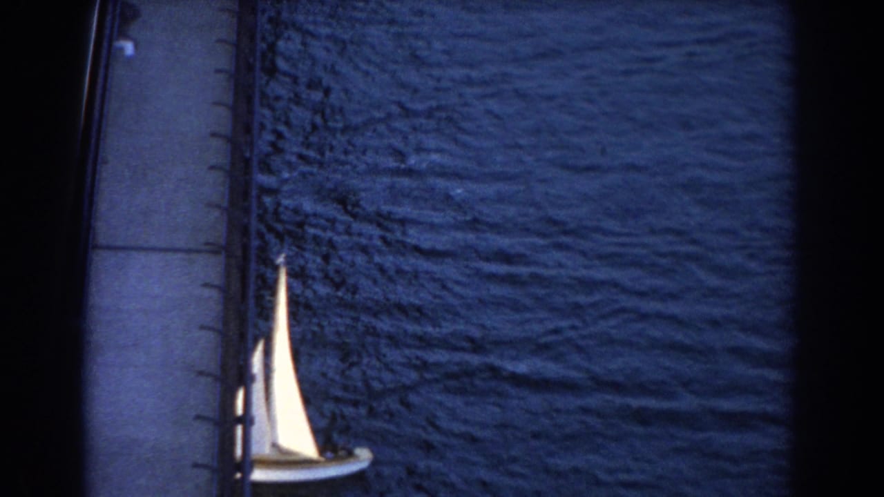 1967 Sydney 8mm frame showing a small sailboat below a bridge, with rippled blue water and dark scan borders.
