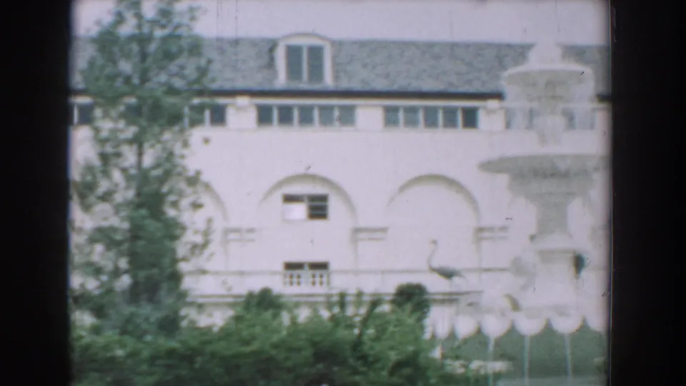 1957 Florida 8mm frame with a large white arched building, landscaping, and part of a decorative fountain visible.
