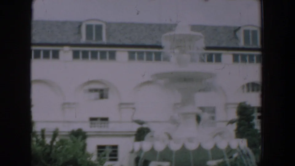 1957 Florida 8mm frame showing a pale fountain form against a white arched building and surrounding greenery.