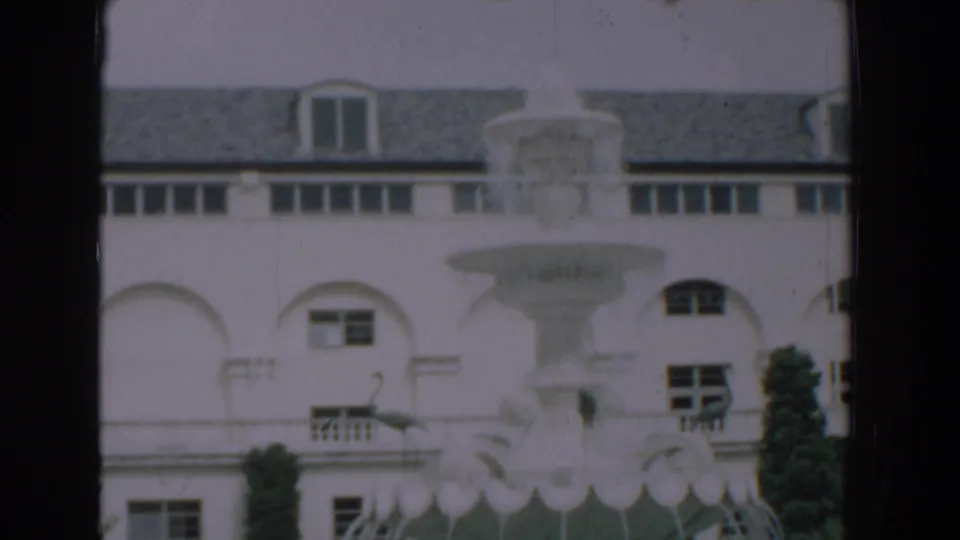 1957 Florida 8mm frame showing the estate fountain, arched white building, and a flamingo near the lower edge.