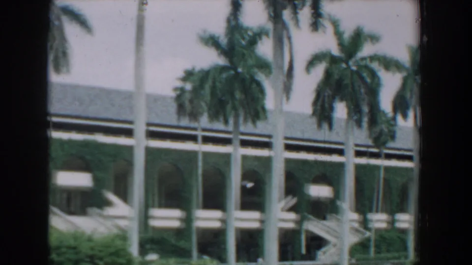 1957 Florida 8mm frame showing palms, lawn, and a large arched building with a green facade and stairs.