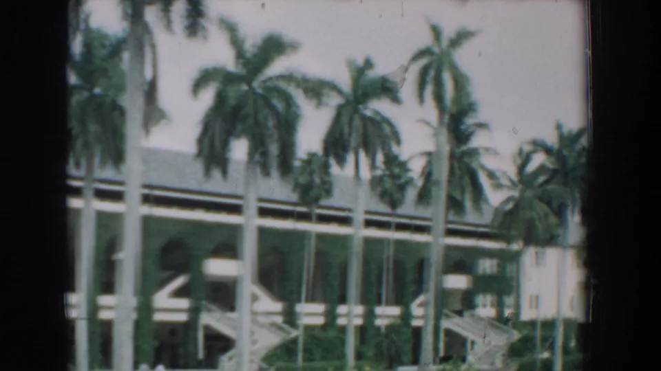 1957 Florida home-movie frame of tall palms in front of a broad arched facade and stairway.