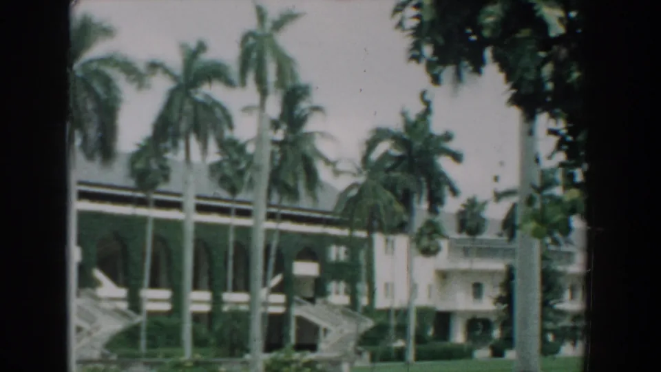 1957 Florida 8mm frame with palms, shrubs, a lawn, and a large arched building seen from outside.