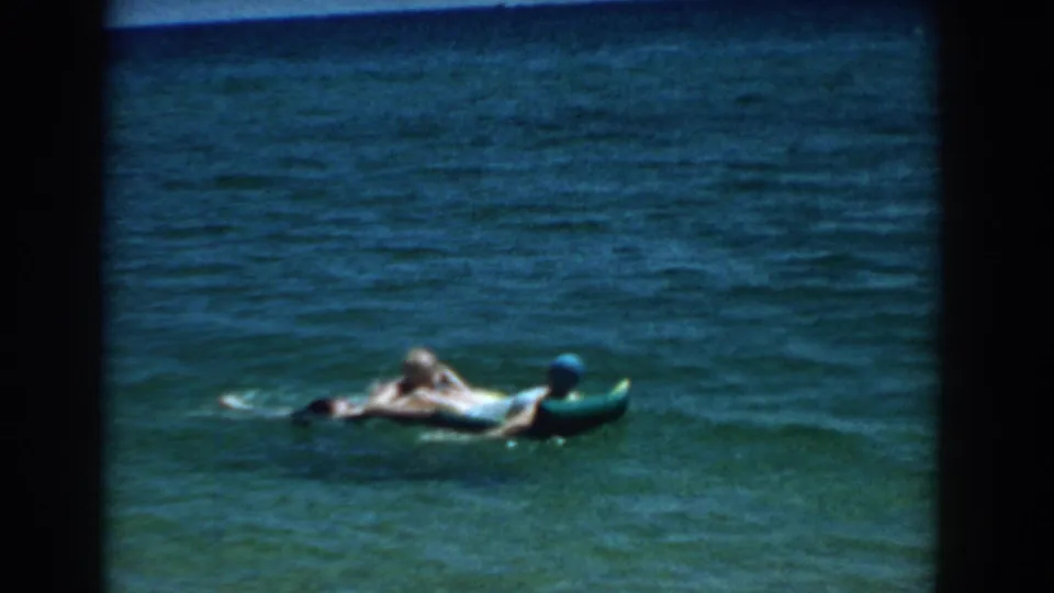 Two people float on an inflatable raft in turquoise Florida ocean water in 1957 home-movie footage.