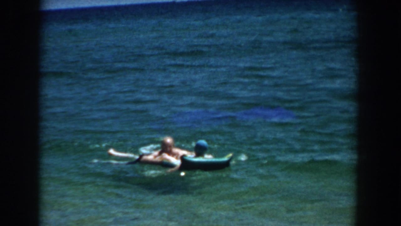 Two people floating beside a blue inflatable raft in open lake water.
