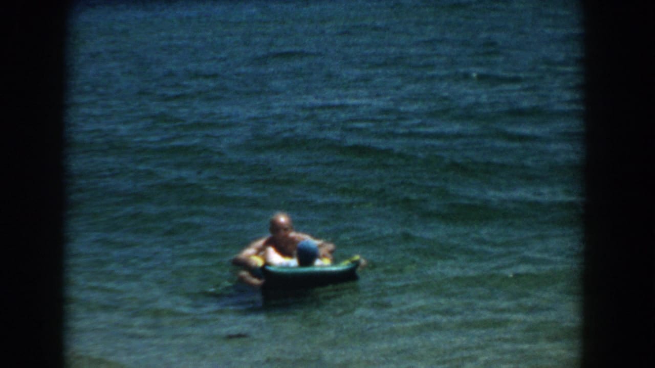 Two adults float in clear blue-green water, partly framed by dark film edges.
