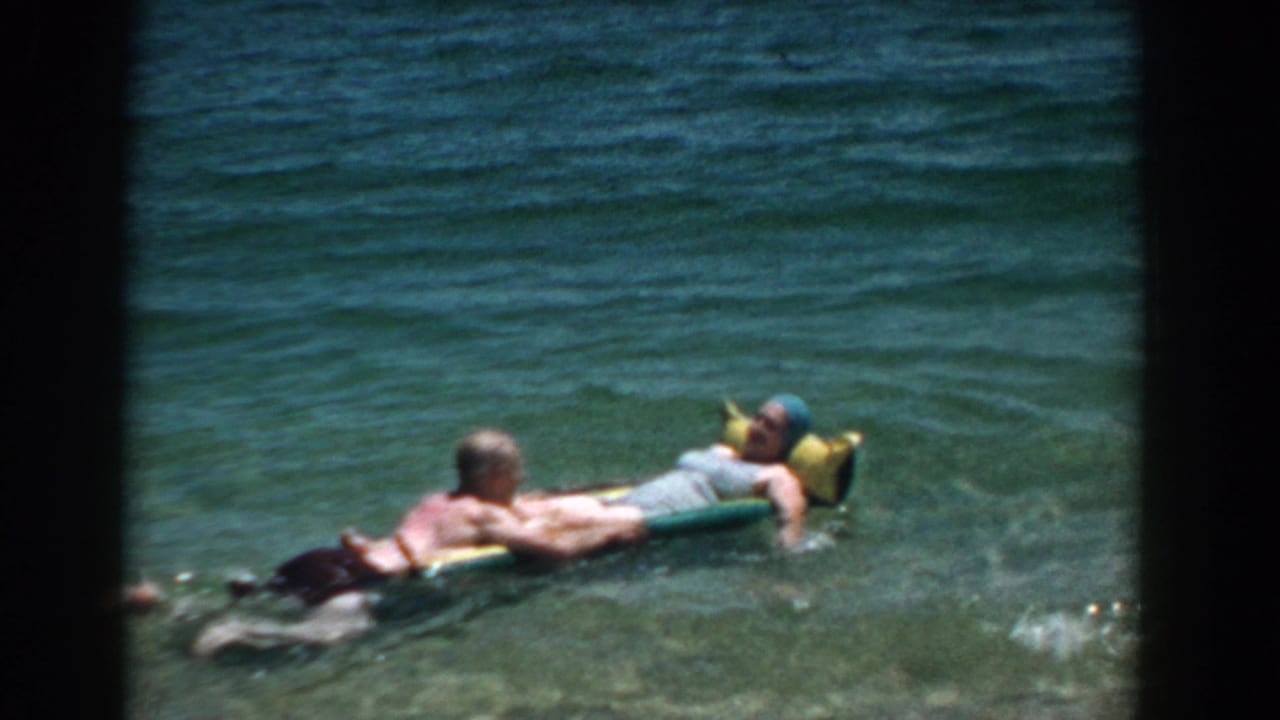 Two adults float in shallow ocean water on an inflatable raft.
