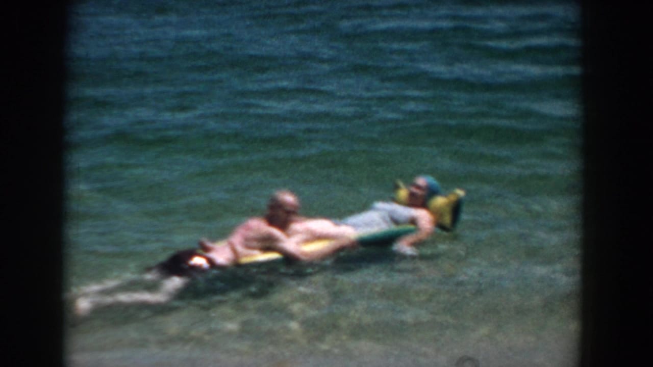 Two adults recline together on a raft in clear ocean water.