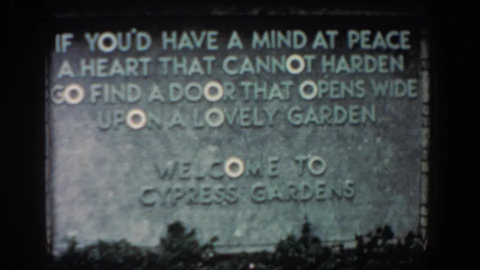 Soft 8mm 1957 Florida view of the Cypress Gardens welcome sign, showing carved lettering, stone texture, and plants below.