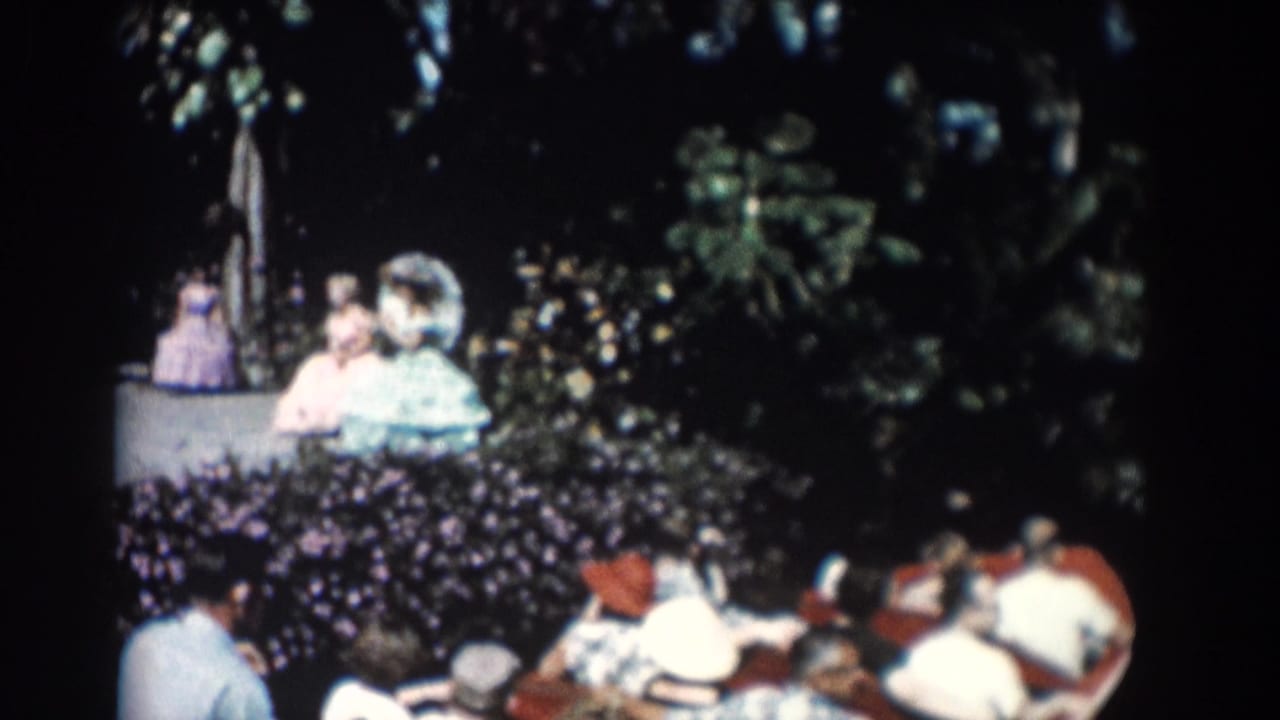 Tourists seated in small boats beside dense garden foliage.