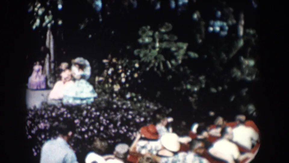 1957 Florida footage frame with tourists seated in boats beside dark trees, shrubs, and tropical garden growth.