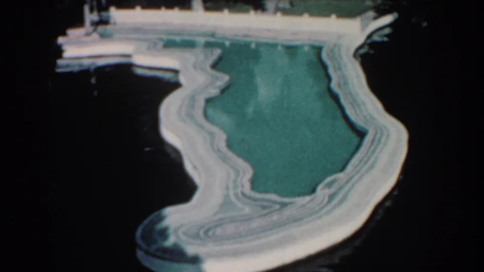 Final frame of the clip holds on the shallow Florida-shaped pool, with white concrete curves, dock details, and dark water around the feature.