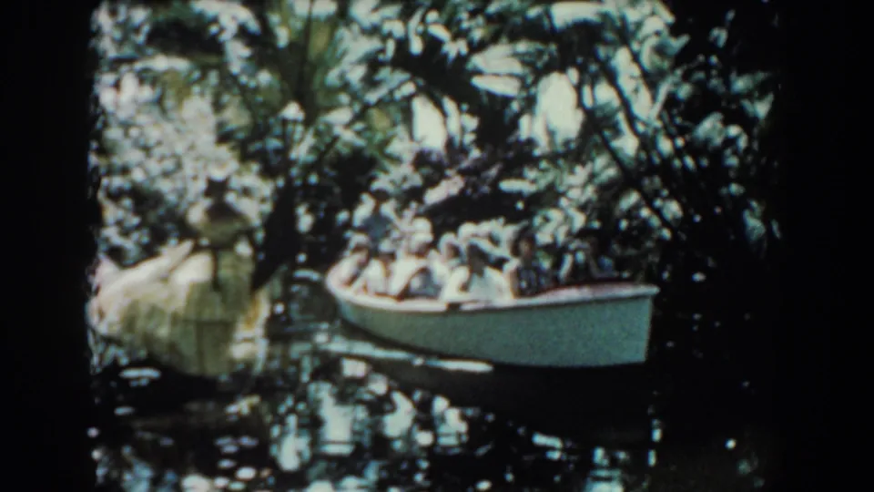 1957 Florida 8mm frame showing passengers in a white boat moving through a shaded swamp waterway.