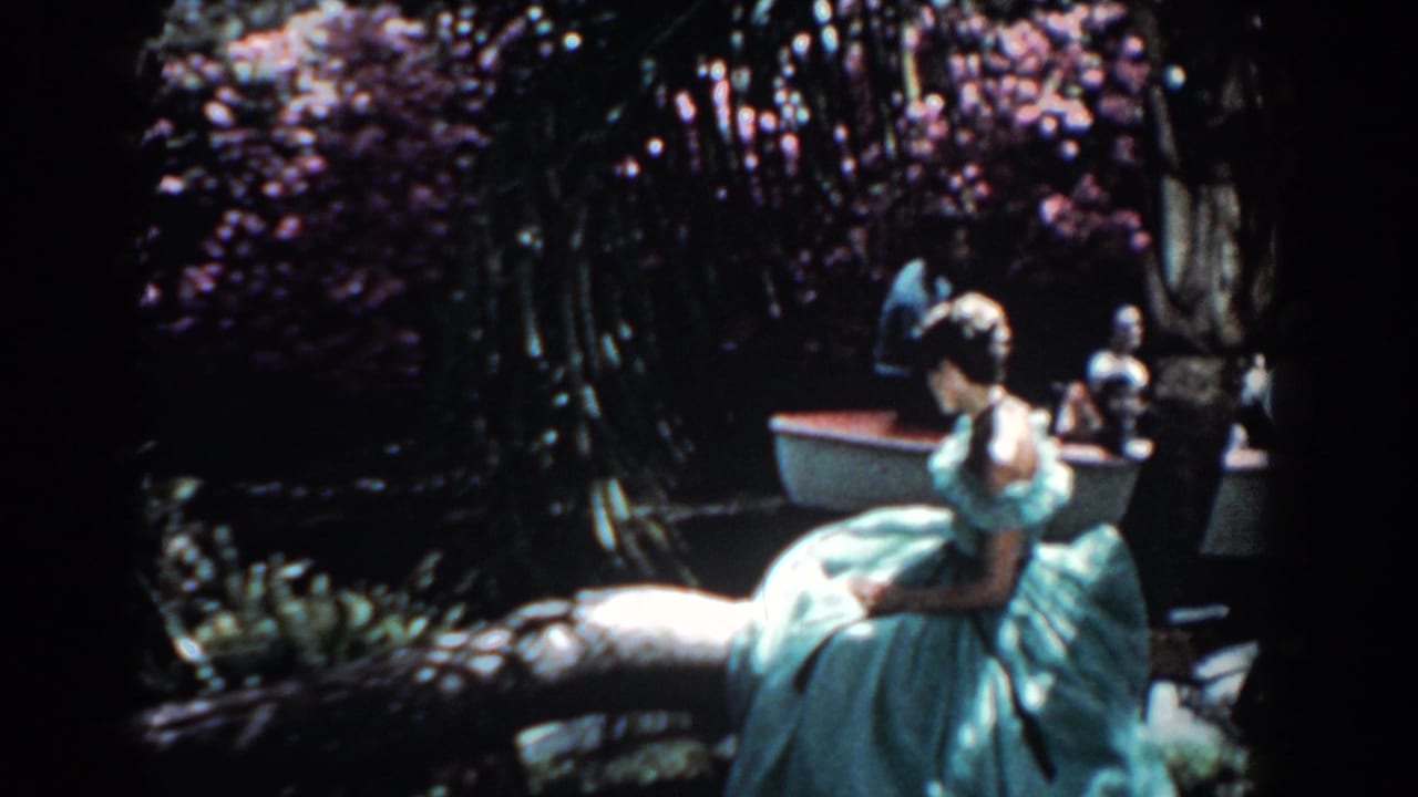 Woman in a pale blue gown sits beside water under flowering trees.