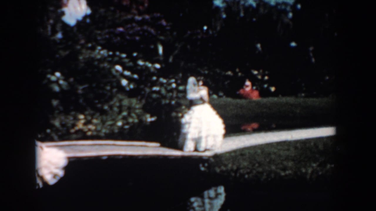 Woman in a white gown walking beside greenery and a low boardwalk edge.