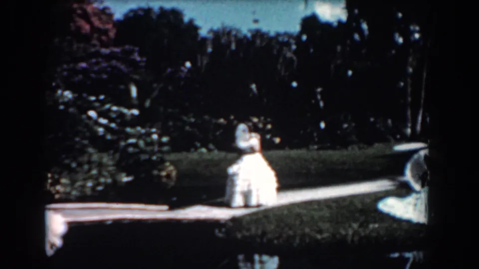 The woman in a white gown stands or walks along a boardwalk-like path in a lush Florida wetland setting.