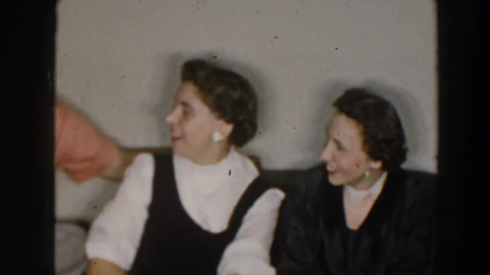 1957 8mm frame identified as Wheeling, Ohio, showing two women seated indoors and looking toward someone outside the left edge of the frame.